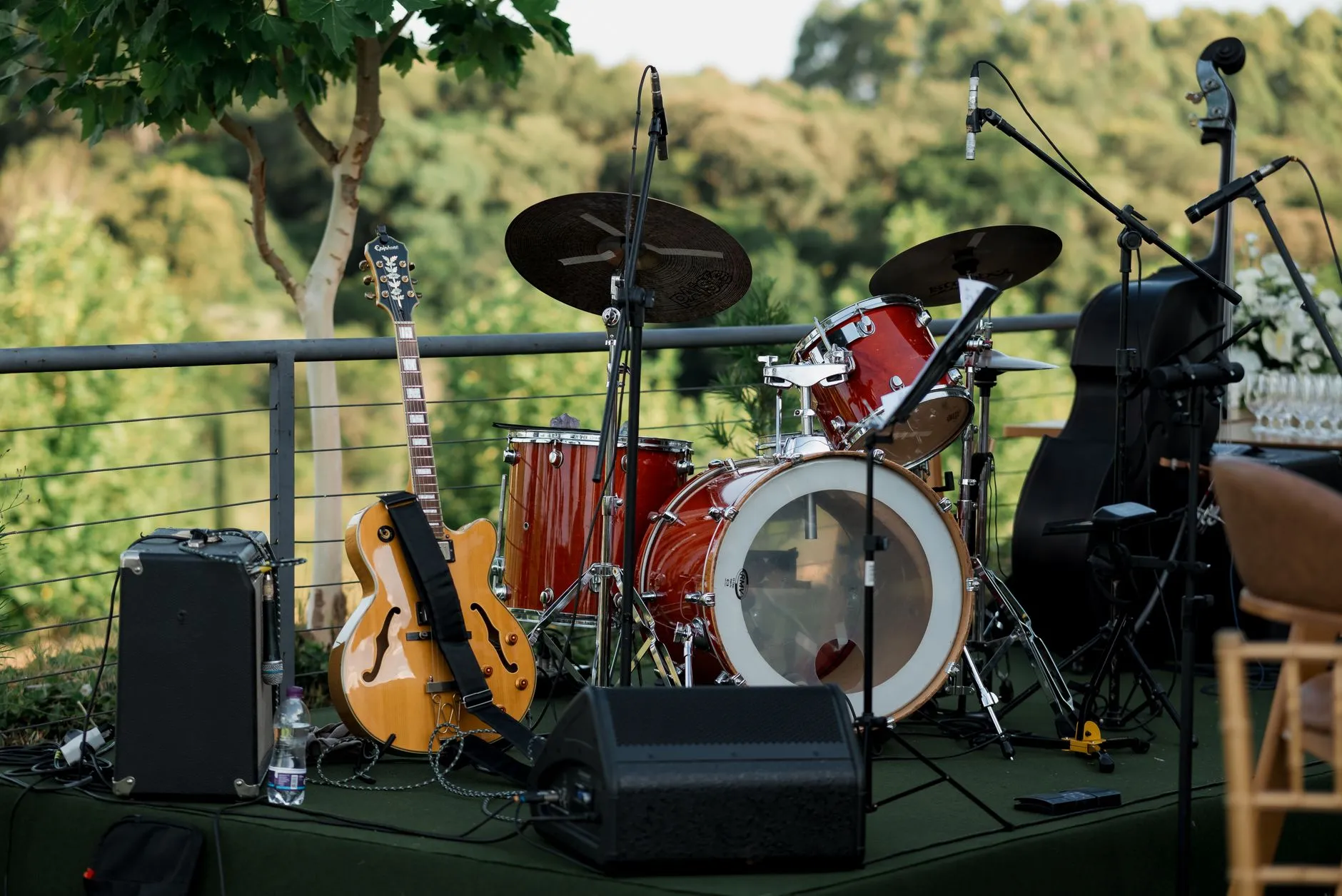 Palco ao ar livre montado para festa, com bateria, guitarra, contrabaixo acústico, microfones e caixas de som