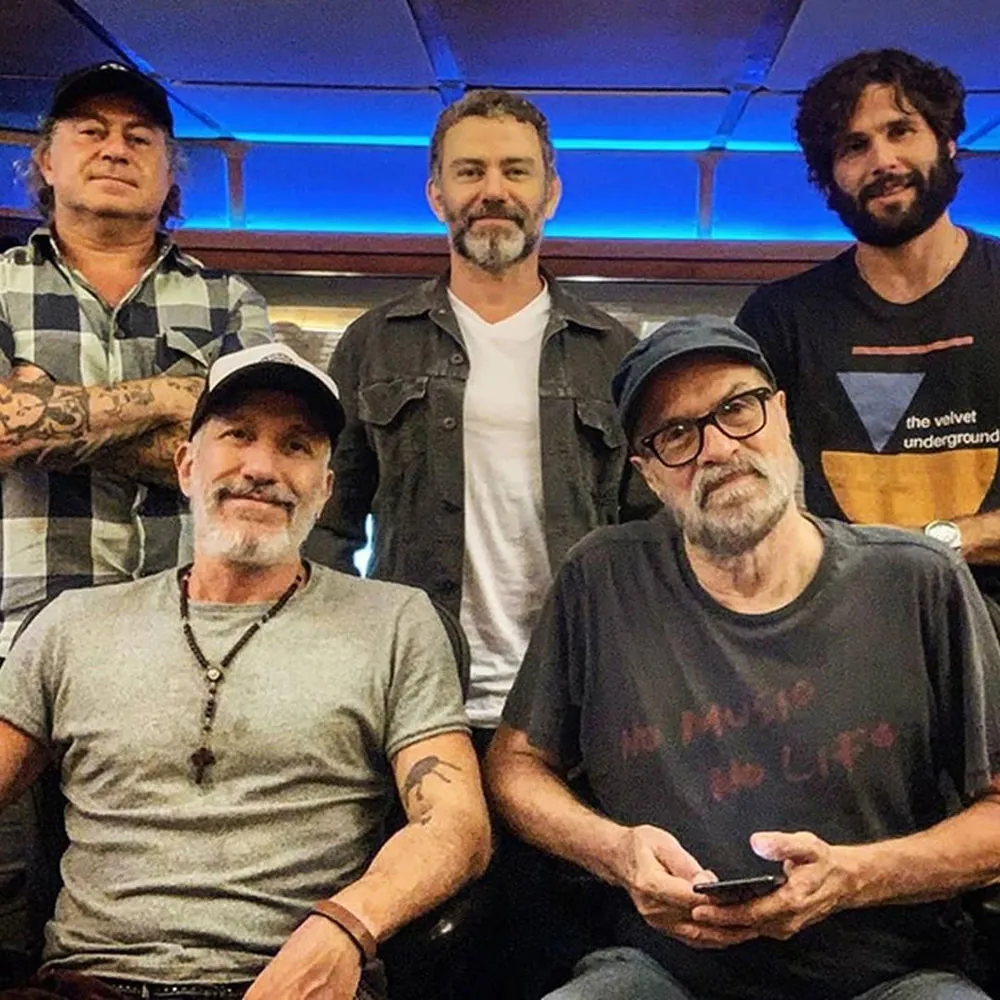 Músicos da Tianastácia reunidos nos bastidores, sob luz azul, antes de um show
